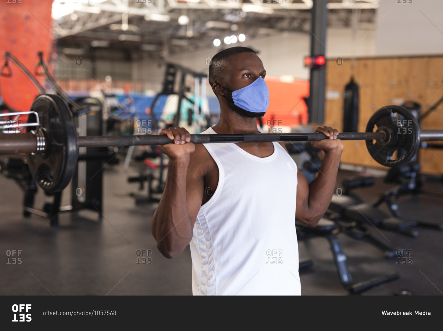 Fit African American man wearing face mask performing exercise with barbell in the gym.