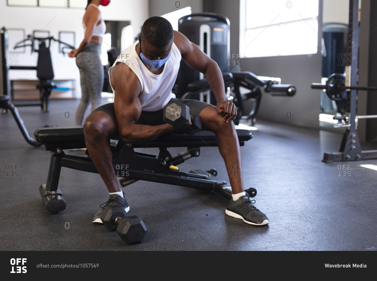 Fit African American man wearing face mask performing exercise with dumbbell in the gym.