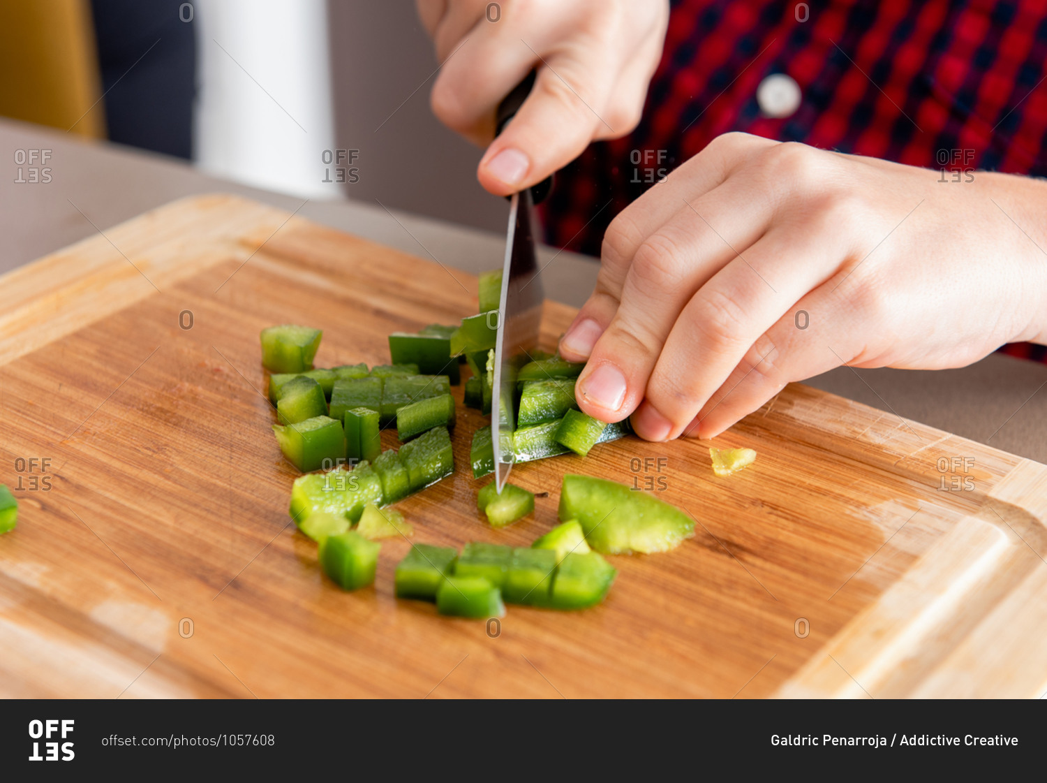 Crop cute little son cut capsicums while cooking with his mother in modern kitchen