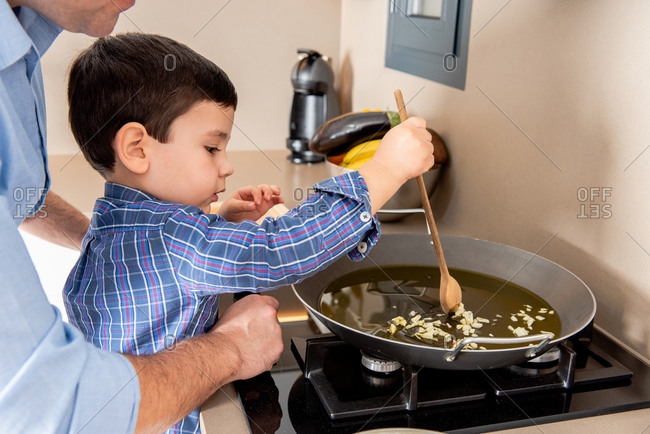 Side view cute concentrated boy stirring garlic on frying pan while learning to cook with father