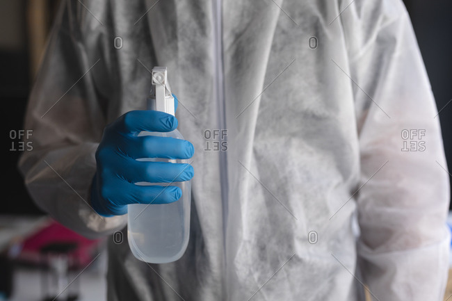 Mid section of health worker in protective clothes holding bottle of disinfectant at modern office.