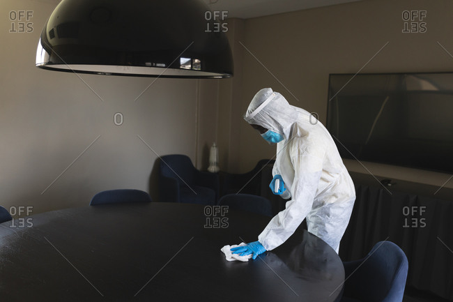 Health worker wearing protective clothes cleaning office using disinfectant spray and cloth.