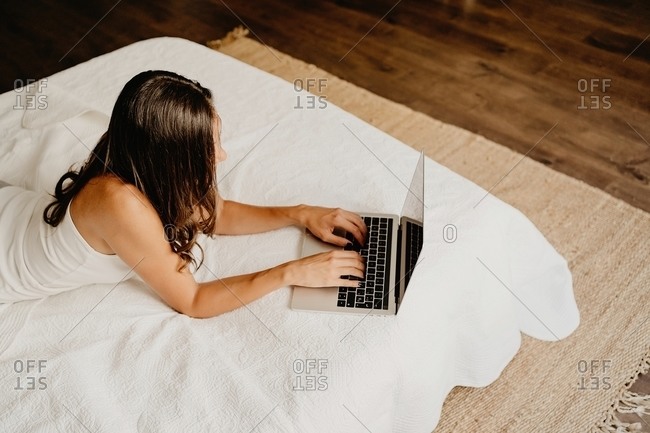 From above cheerful millennial female in nightwear lying on bed and surfing internet