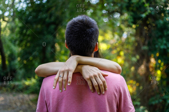 Back view unrecognizable man embracing girlfriend while standing face to face in abundant summer park