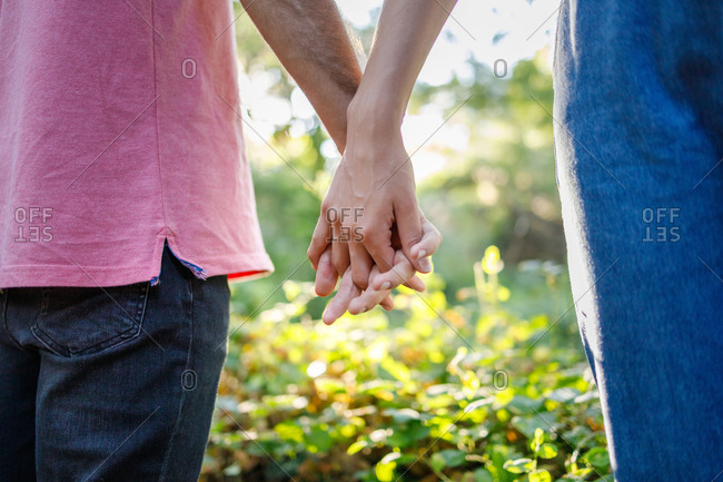 Crop anonymous romantic couple holding hands gently while spending time together in abundant lush nature on sunny weather