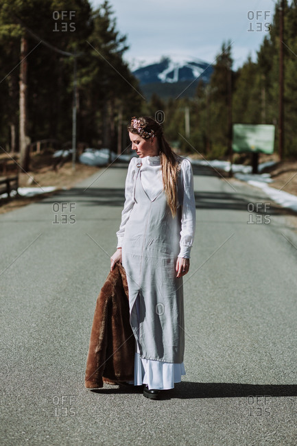 Full length serene thoughtful female in white loose dress standing with coat in hand