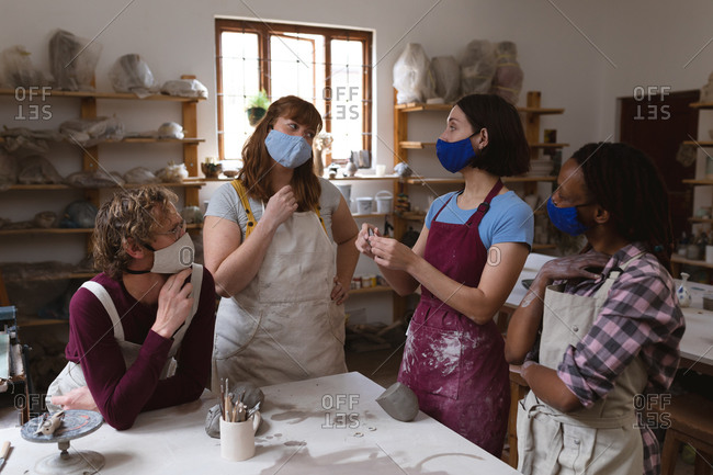 Multi-ethnic group of potters in face masks working in pottery studio.