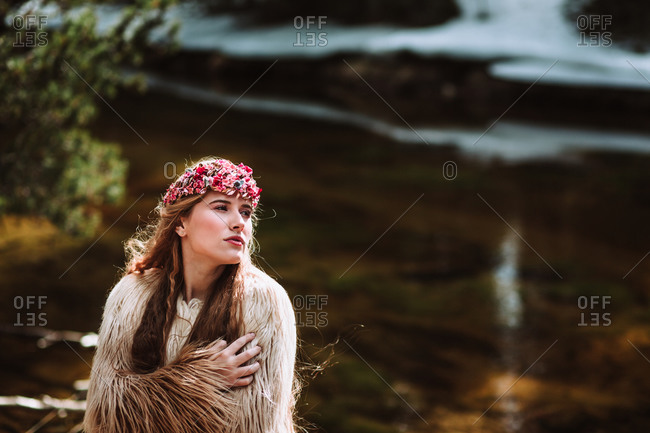 Charming young long haired female in nordic style boho clothes and wreath strolling along river shore