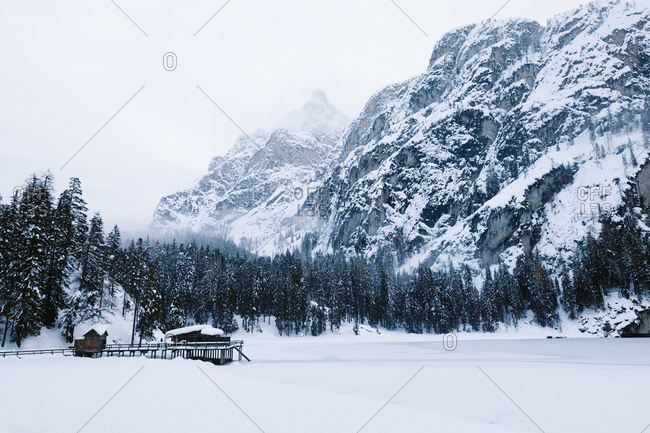 Cold winter landscape with lonely stilt house located near frozen river in snowy mountain valley in dense snowstorm