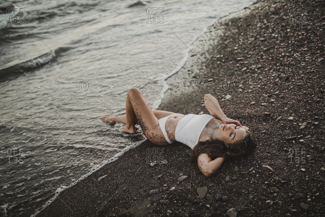 Young sexy girl in sequins and swimsuit lying in the water on the beach