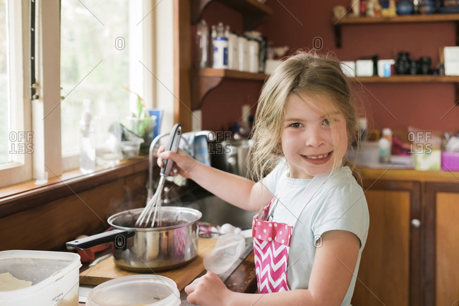 Young girl smiling and mixing hot baking mixture in messy kitchen
