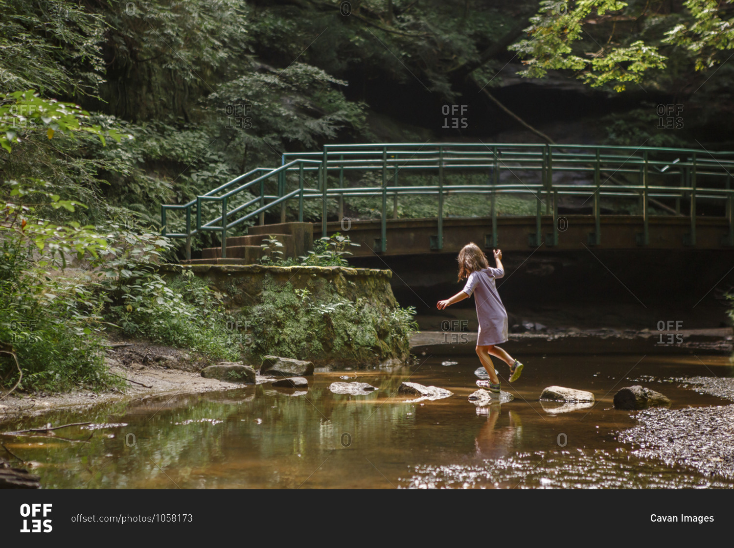 A little girl balances on stepping stones across a stream in woods