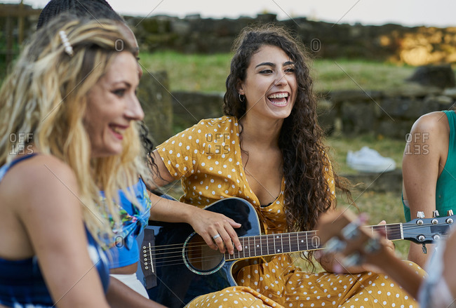 Smiling woman playing guitar having fun with group of friends