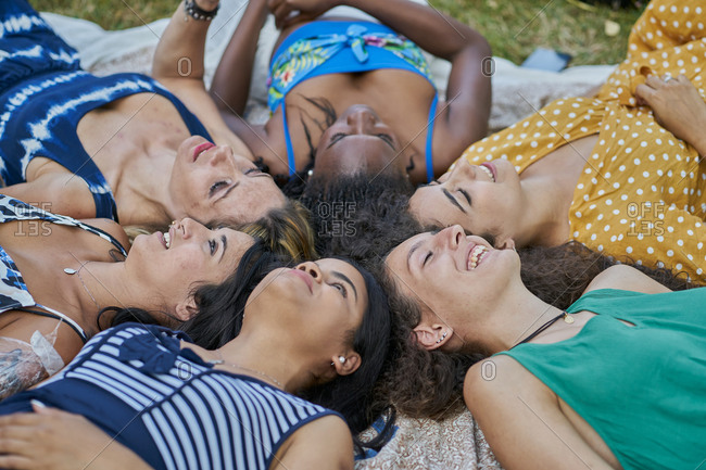 Group of smiling female friends laying on a towel in a park having fun