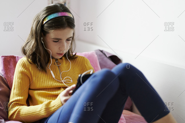 Girl lying on her bed looking at a tablet and wearing headphones