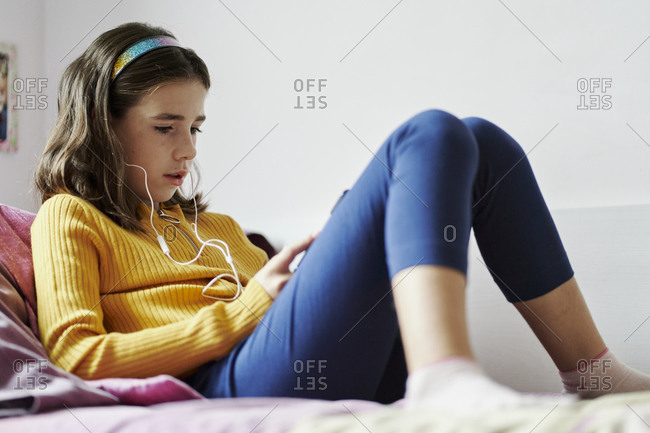 Girl lying on her bed looking at a tablet and wearing headphones