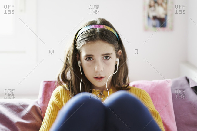 Front view of a girl lying on her bed looking at camera with headphones