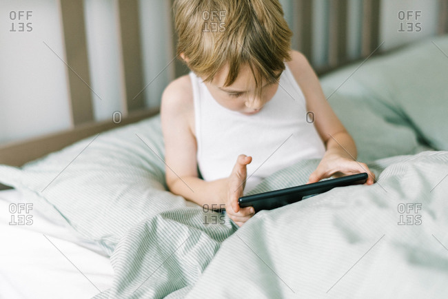 Little boy waking up in the morning playing his tablet