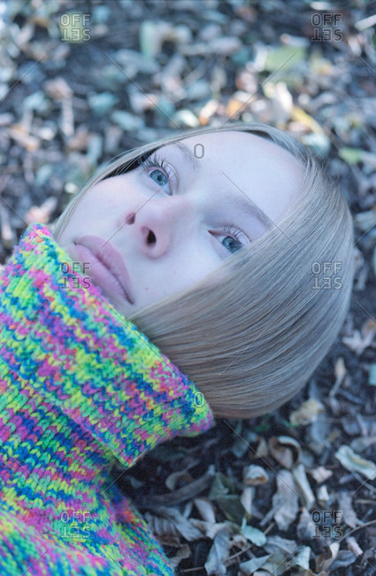 Close-up of a young woman in a sweater lying in the autumn forest.