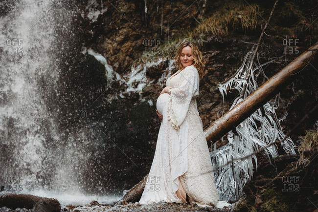 Expecting woman looking down standing next to a waterfall in winter