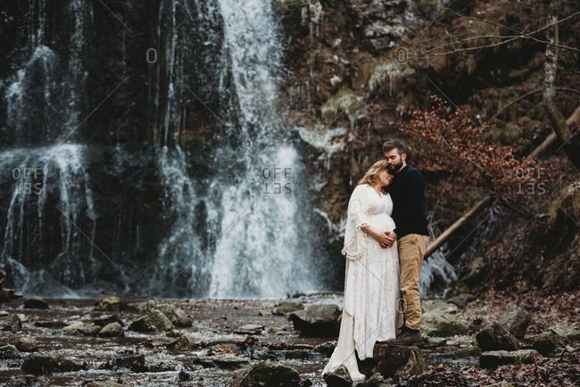 Husband and expecting wife outside in winter by a waterfall in winter