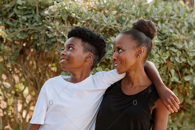 Smiling preteen black boy with arm draped around happy mom looking up