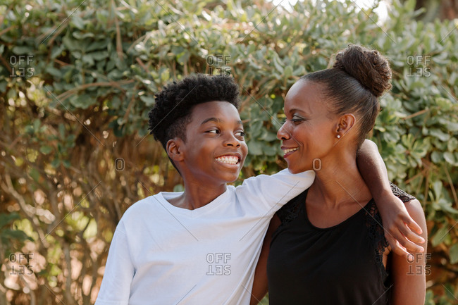 Smiling black preteen boy with arm around shoulder of happy mom