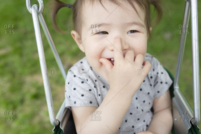 Adorable Baby Girl Smiles with Hand Over Mouth While Swinging Outdoors