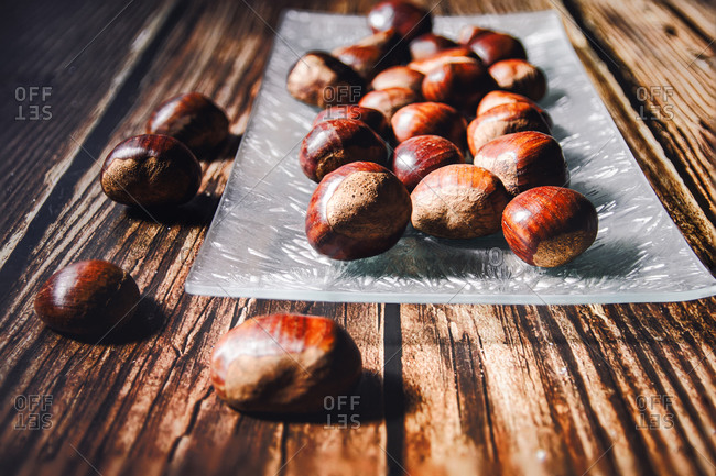 Close-up of several chestnuts in a glass dish, on a wooden table.