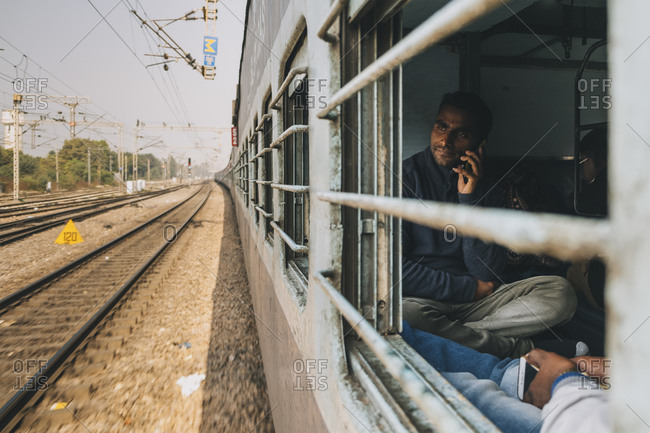 Agra, UP, India - January 21, 2018: Young man talking on the mobile phone while commuting from New Delhi to Agra, Sleeper Class train.
