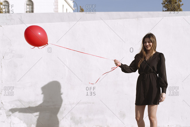Young woman carries a red gas balloon in front of a white wall