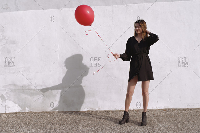 Young woman carries a red gas balloon in front of a white wall