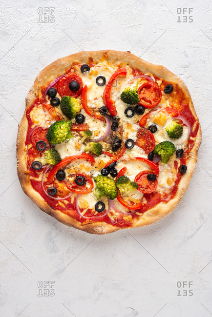 Overhead view of fresh whole pizza with mozzarella cheese, broccoli, tomatoes, red onion, olives and paprika