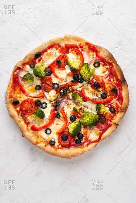 Overhead view of fresh sliced pizza with mozzarella cheese, broccoli, tomatoes, red onion, olives and paprika