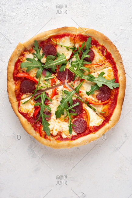 Overhead view of fresh sliced pizza with sausage, mozzarella cheese, arugula and paprika