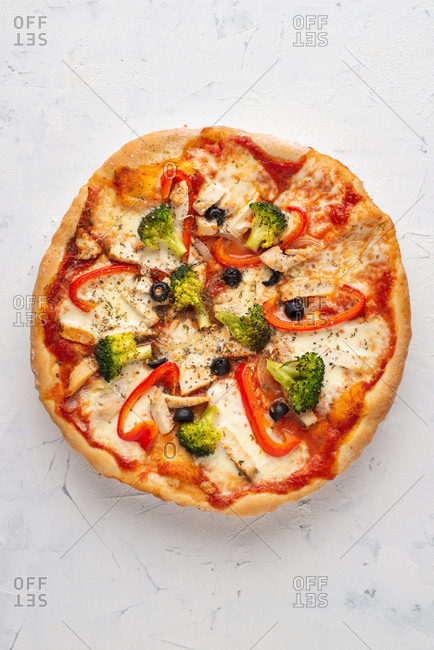 Overhead view of fresh pizza with white chicken meat, olives and broccoli served on white ceramic plate