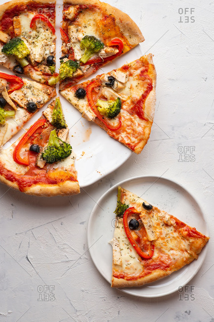 Overhead view of fresh sliced pizza with white chicken meat, olives and broccoli served on white ceramic plate