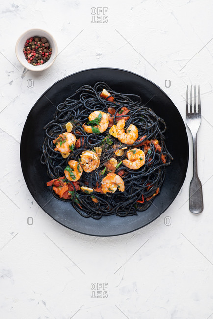 Black squid ink pasta with red tomato sauce and shrimps served on black plate