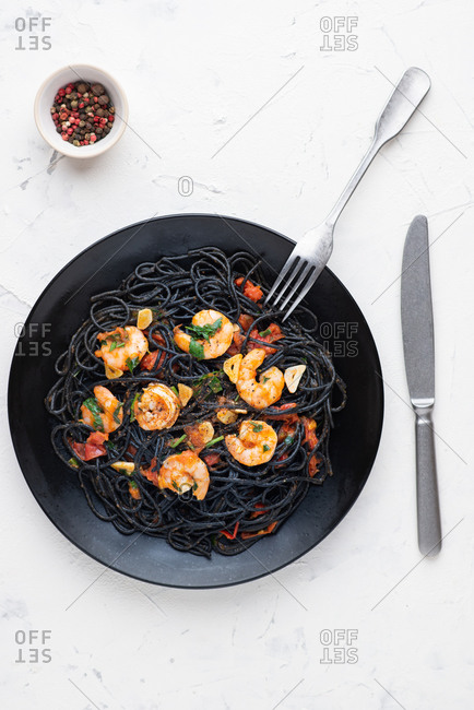 Black squid ink pasta with red tomato sauce and shrimps served on black plate