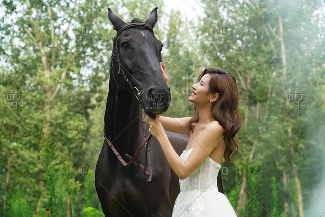 Outdoor wear wedding dress beautiful young women touching the horse