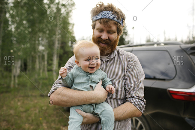 USA, Utah, Uinta National Park, Smiling man holding baby son (6-11 months) in field, car in background