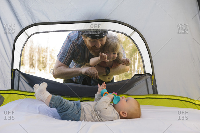 USA, Utah, Uinta National Park, Father and daughter (2-3) peeking into tent and looking at baby boy (6-11 months) inside
