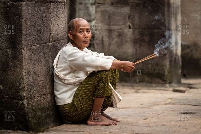 SIEM REAP, CAMBODIA - 10 AUGUST 2013: Nun prays with incense sticks in Bayon Temple in Angkor Thom.