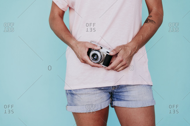 Midsection of woman holding old-fashioned camera while standing against turquoise background