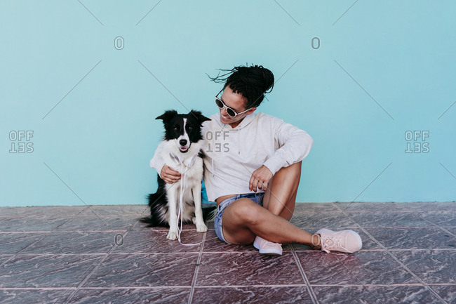 Happy woman sitting with arm around Border Collie dog against turquoise wall
