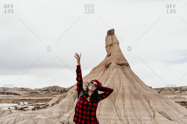 Spain- Navarre- Portrait of female tourist standing with raised arms in front of sandstone rock formation in Bardenas Reales