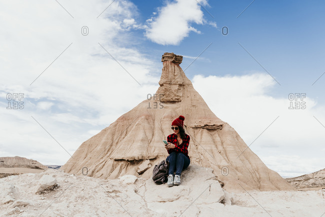 Spain- Navarre- Female tourist using smart phone in front of sandstone rock formation in Bardenas Reales