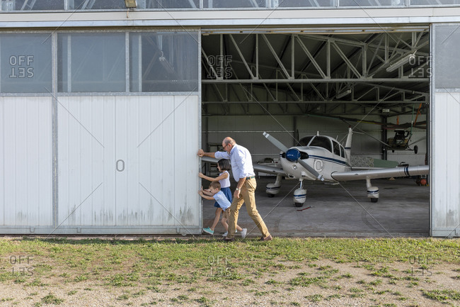 Children and grandfather opening door of airplane hangar