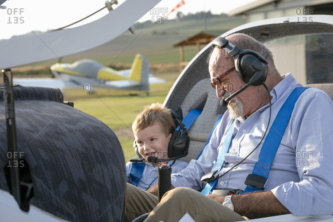 Grandson and grandfather sitting inside airplane at airfield