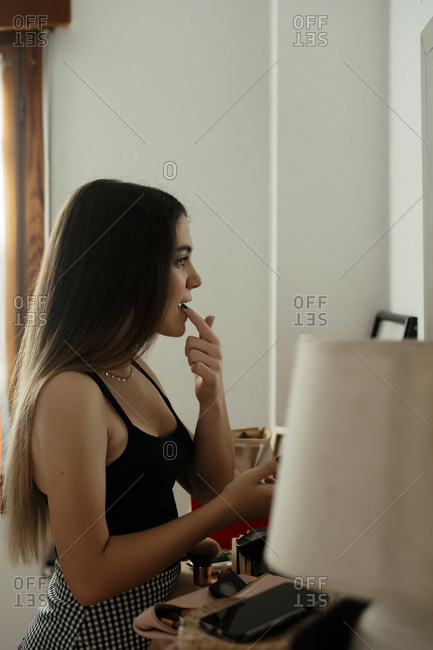 Teenager girl applying lipstick while standing at home